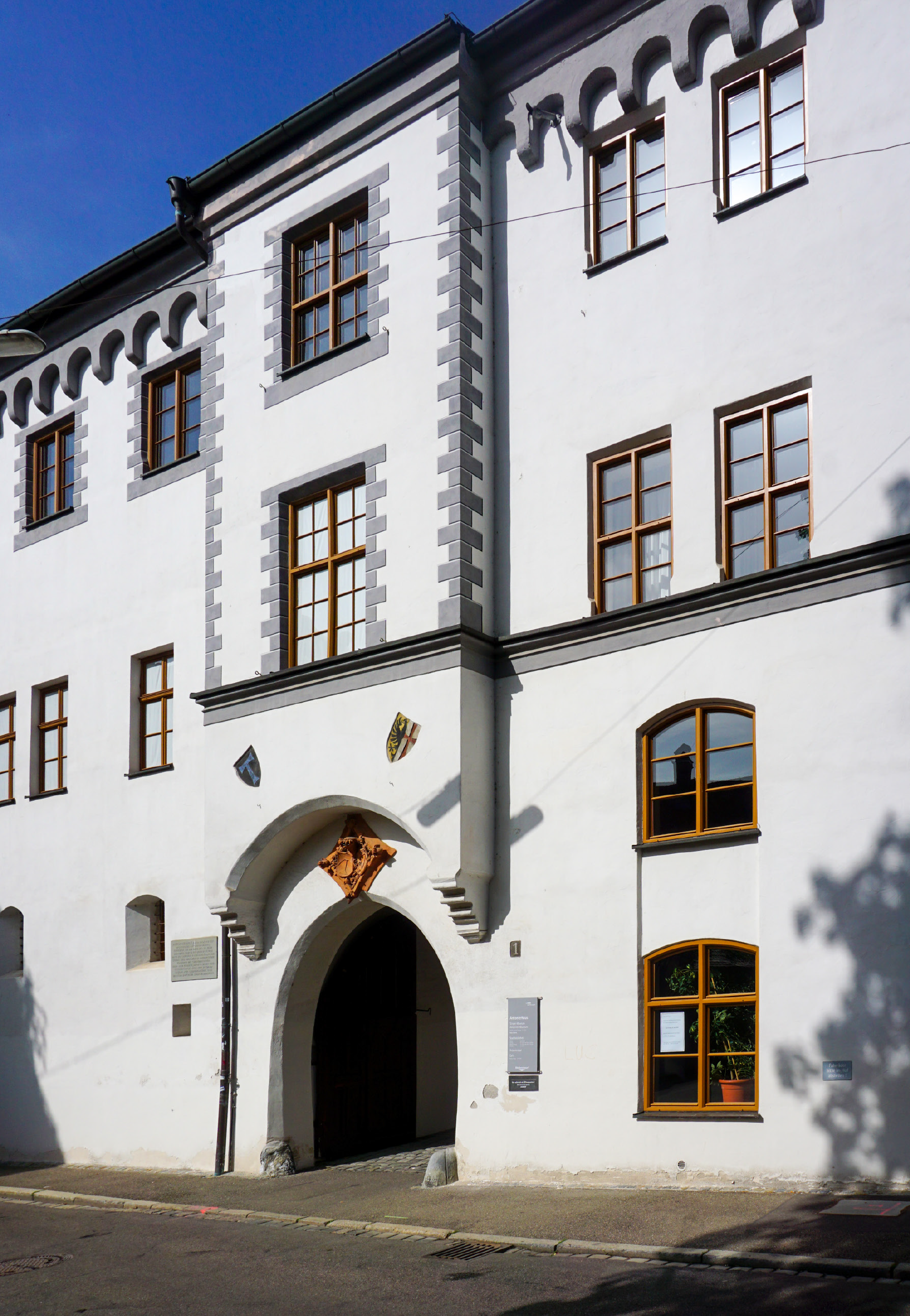 Ein Ausschnitt der weißen Fassade des mittelalterlichen Antonierhauses mit vielen kleinen Holzfenstern, mittig die runde Toreinfahrt.